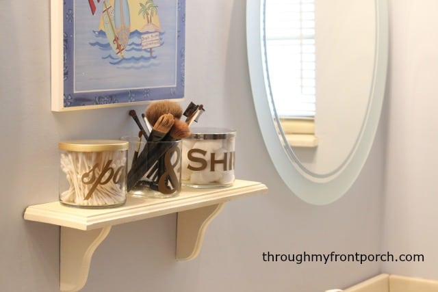 Candle jars on a shelf with a mirror next to them.
