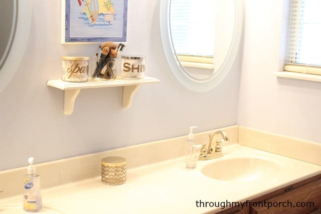 Candle jars on a white shelf with the bathroom counter below.