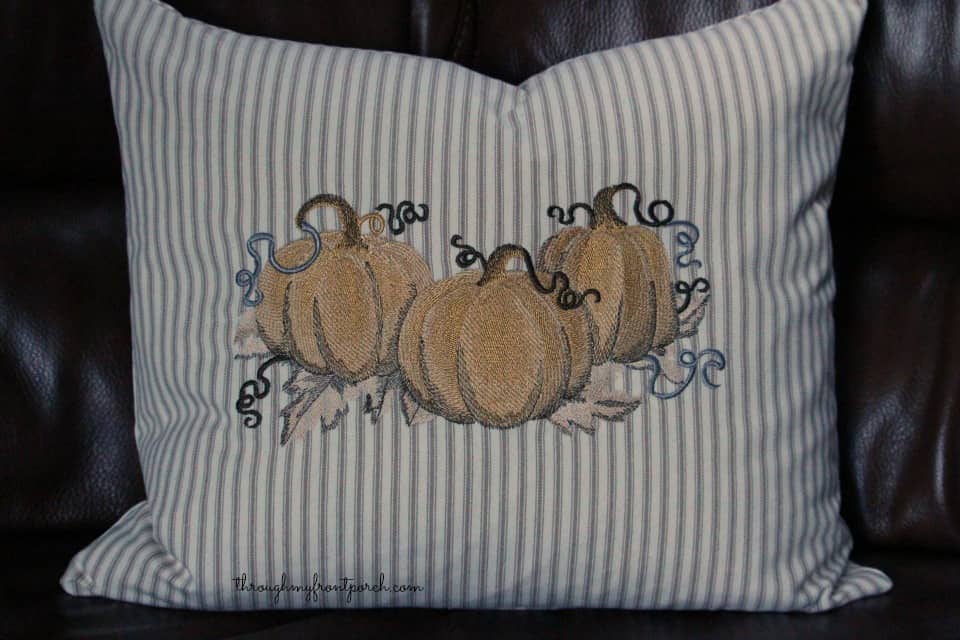Pillow with embroidered pumpkins on couch.
