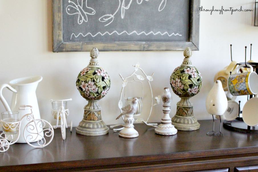 Spring decor of bird figures, topiary, candle holders, and a pitcher on a sideboard.