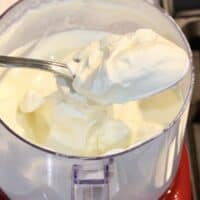Whipped cream on spoon on top of food chopper bowl.