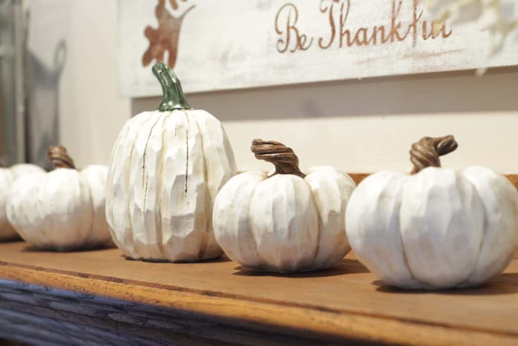 White pumpkins sitting on a mantle in front of a sign.