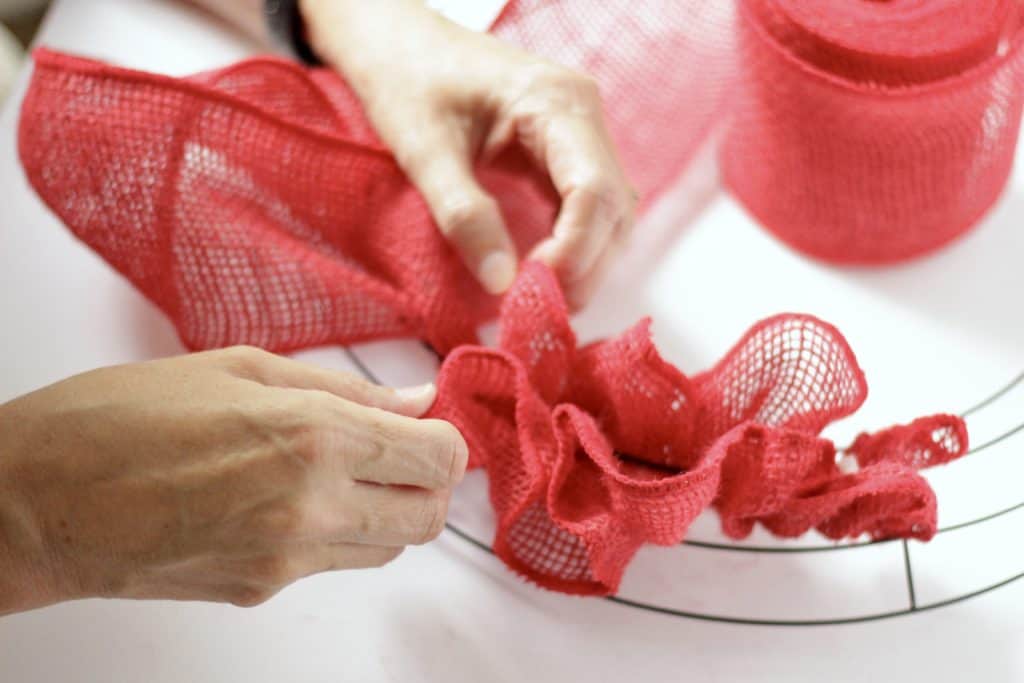Hands tying ribbon onto the wreath frame.