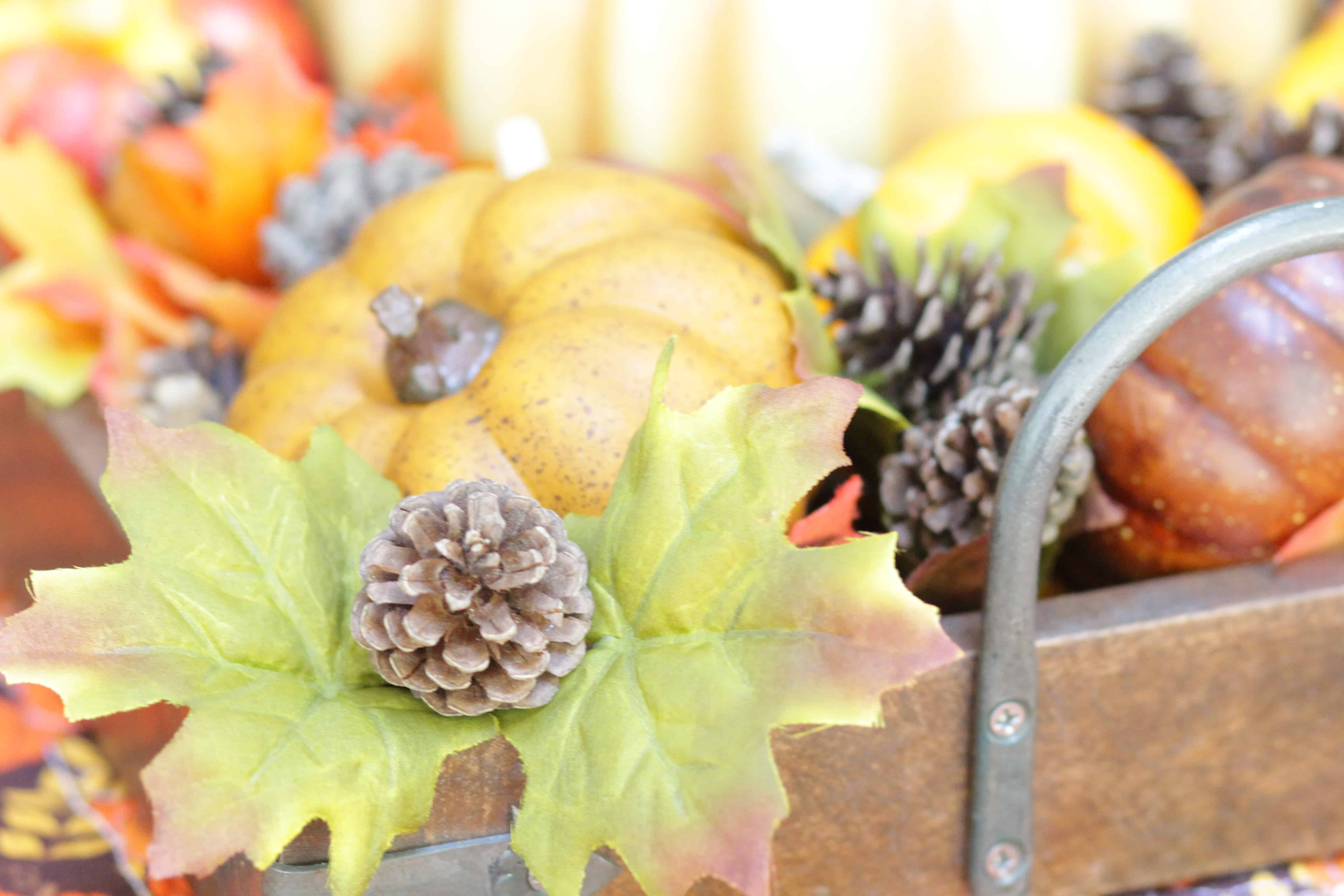 A closeup of pumpkins ,leaves and acorns in a wooden tray with metal handle.