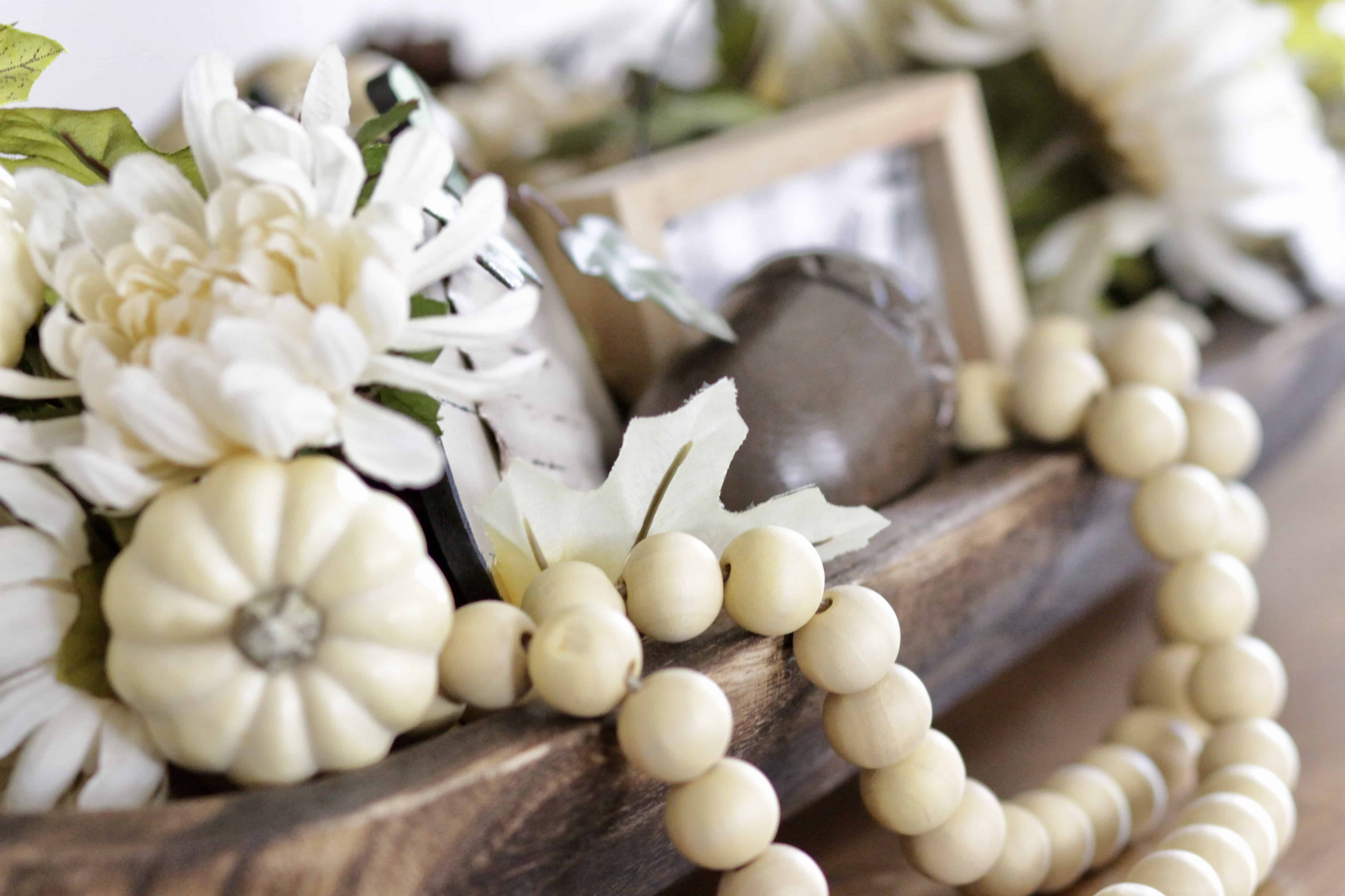 A dough bowl filled with wooden beads, pumpkins and foliage.