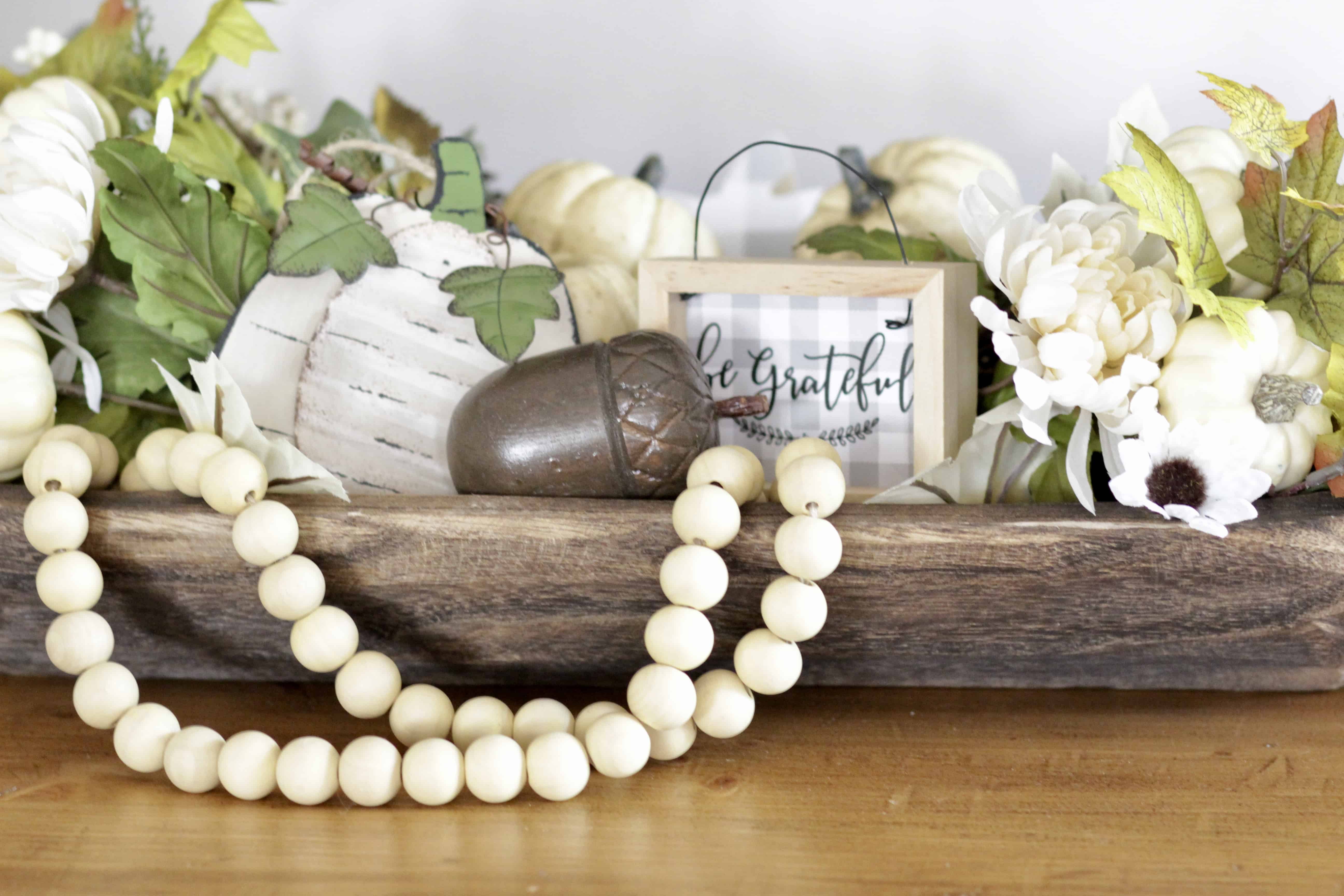 A fall dough bowl filled with leaves, pumpkins and wooden beads.