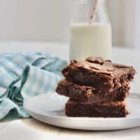 A stack of brownies beside a napkin with a bottle of milk.