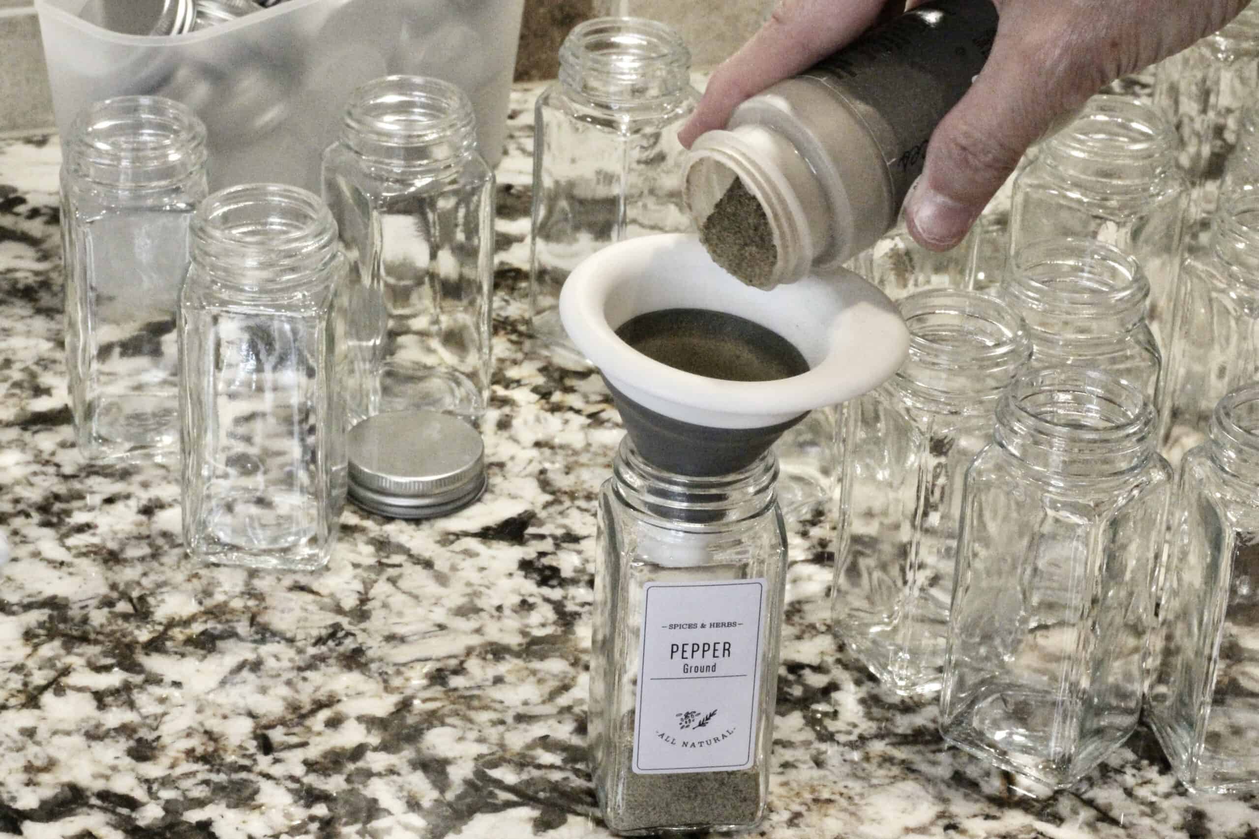 Filling a spice jar with pepper on the kitchen counter using a small funnel.