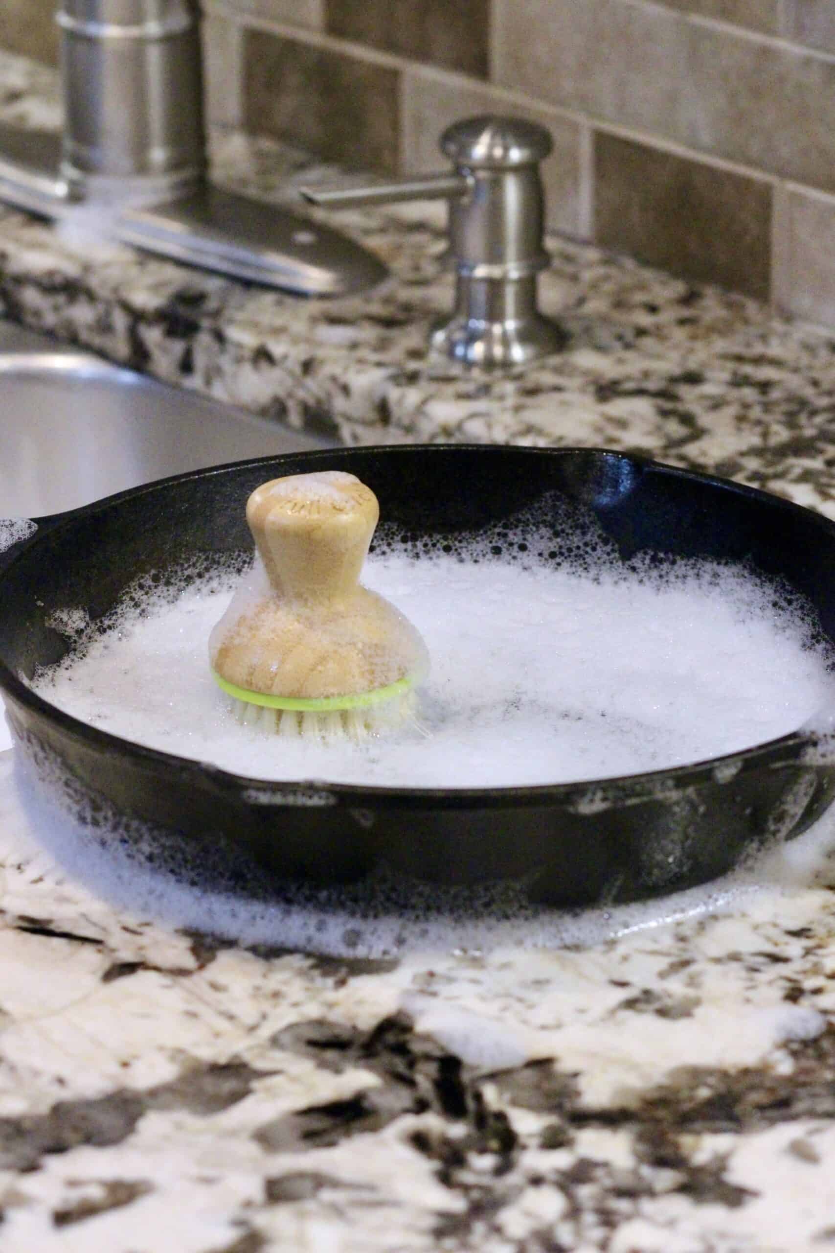 A scrub brush in a cast iron skillet filled with bubbles.