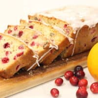 Cranberry orange bread on a board with an orange and cranberries.