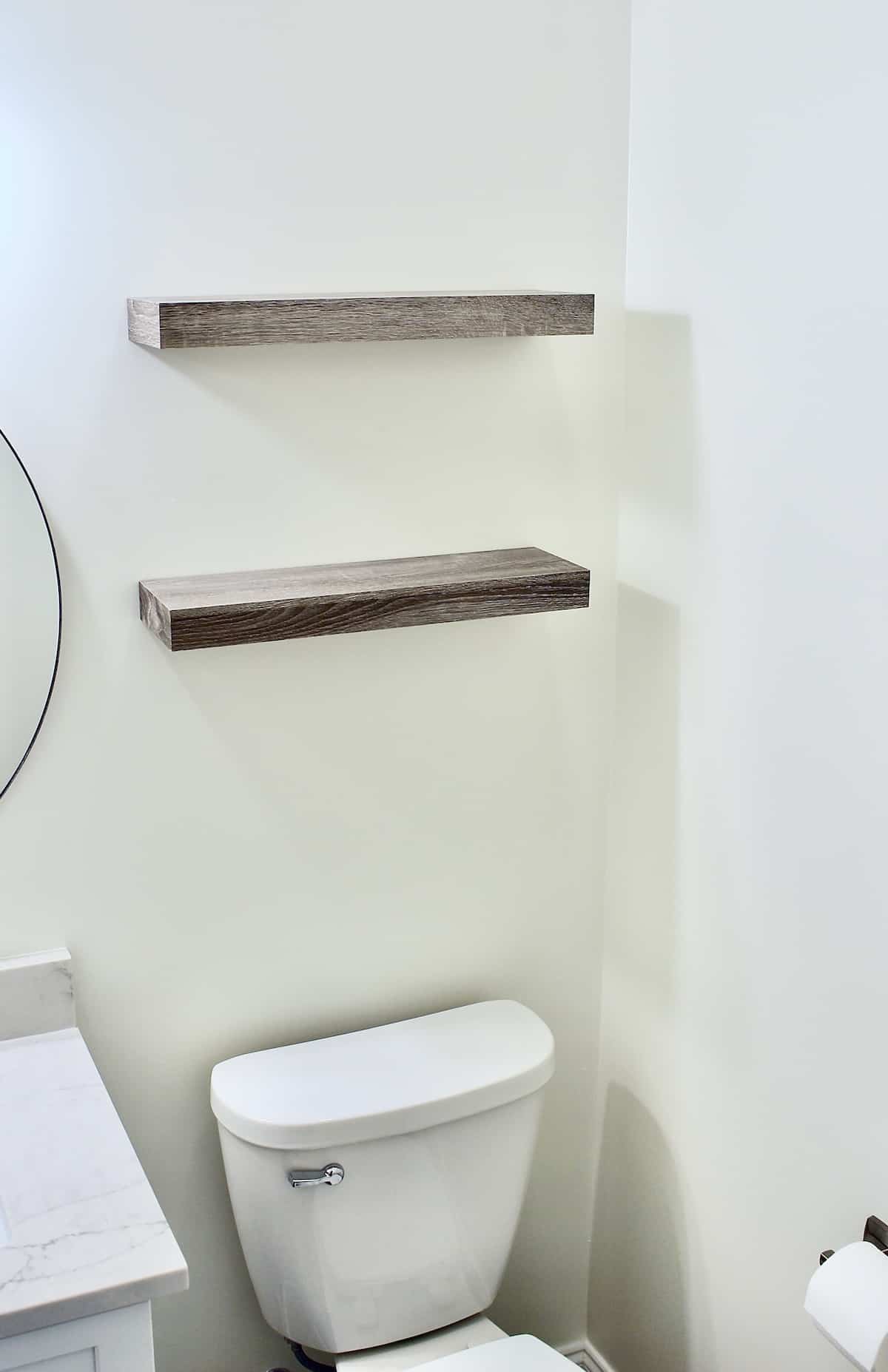 Two floating shelves over a toilet with a partial view of sink and mirror.
