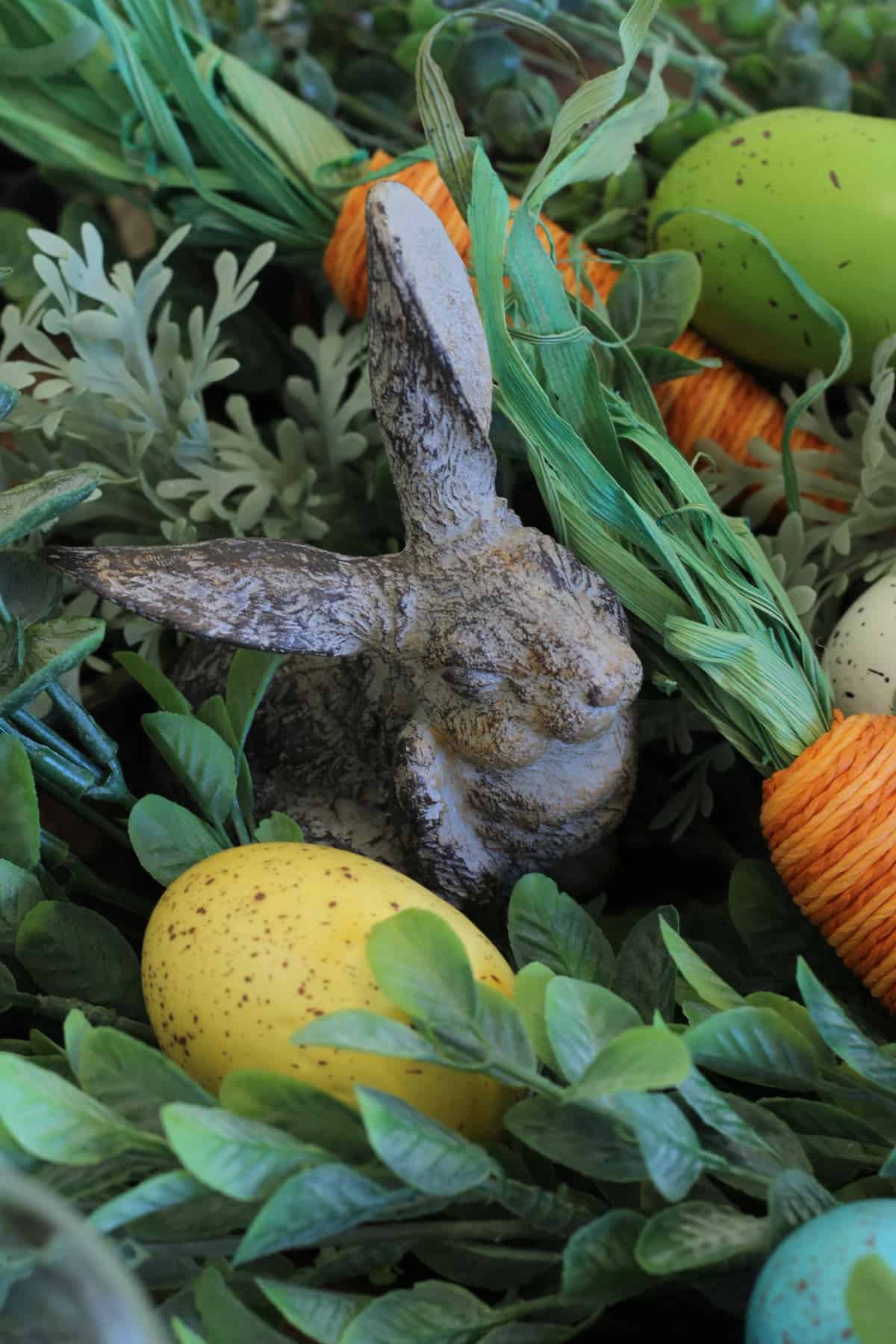 A cast iron bunny in greenery with speckled eggs and faux carrots.