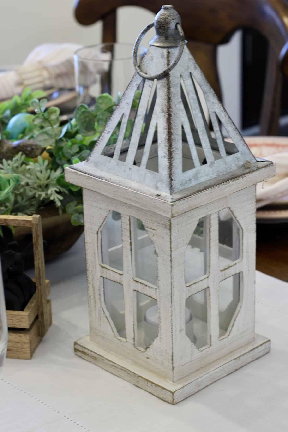 A lantern with a galvanized top on a table with decor pieces.