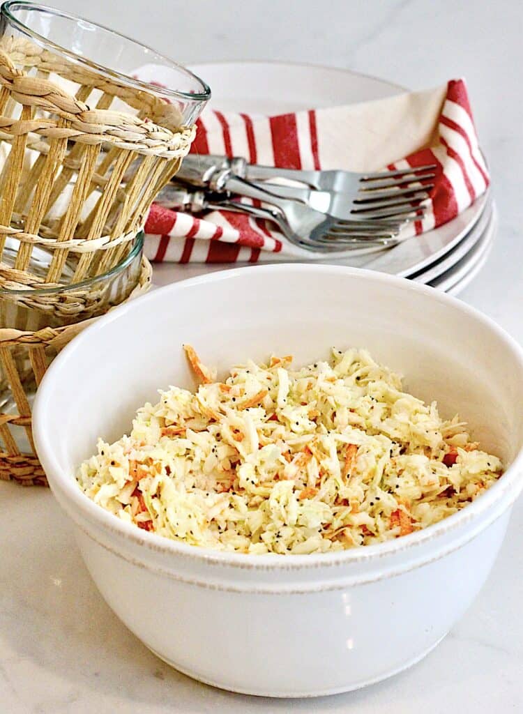 Two glasses with plates, forks, and napkins next to a bowl of coleslaw.