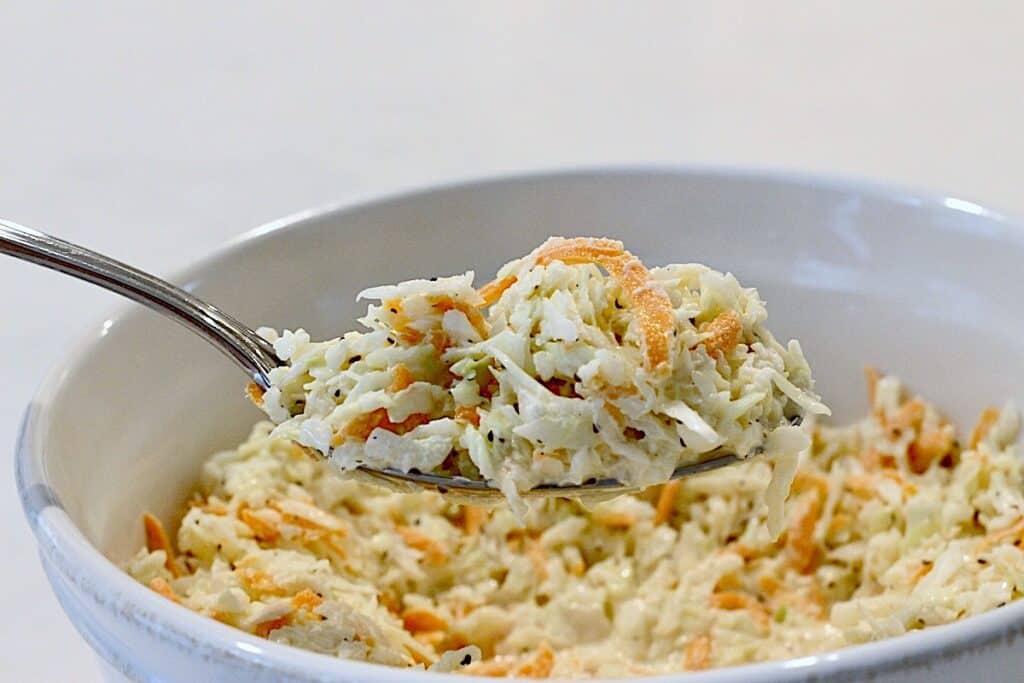 A spoonful of coleslaw above a white bowl.