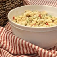 A bowl of macaroni salad on a striped napkin next to a basket.