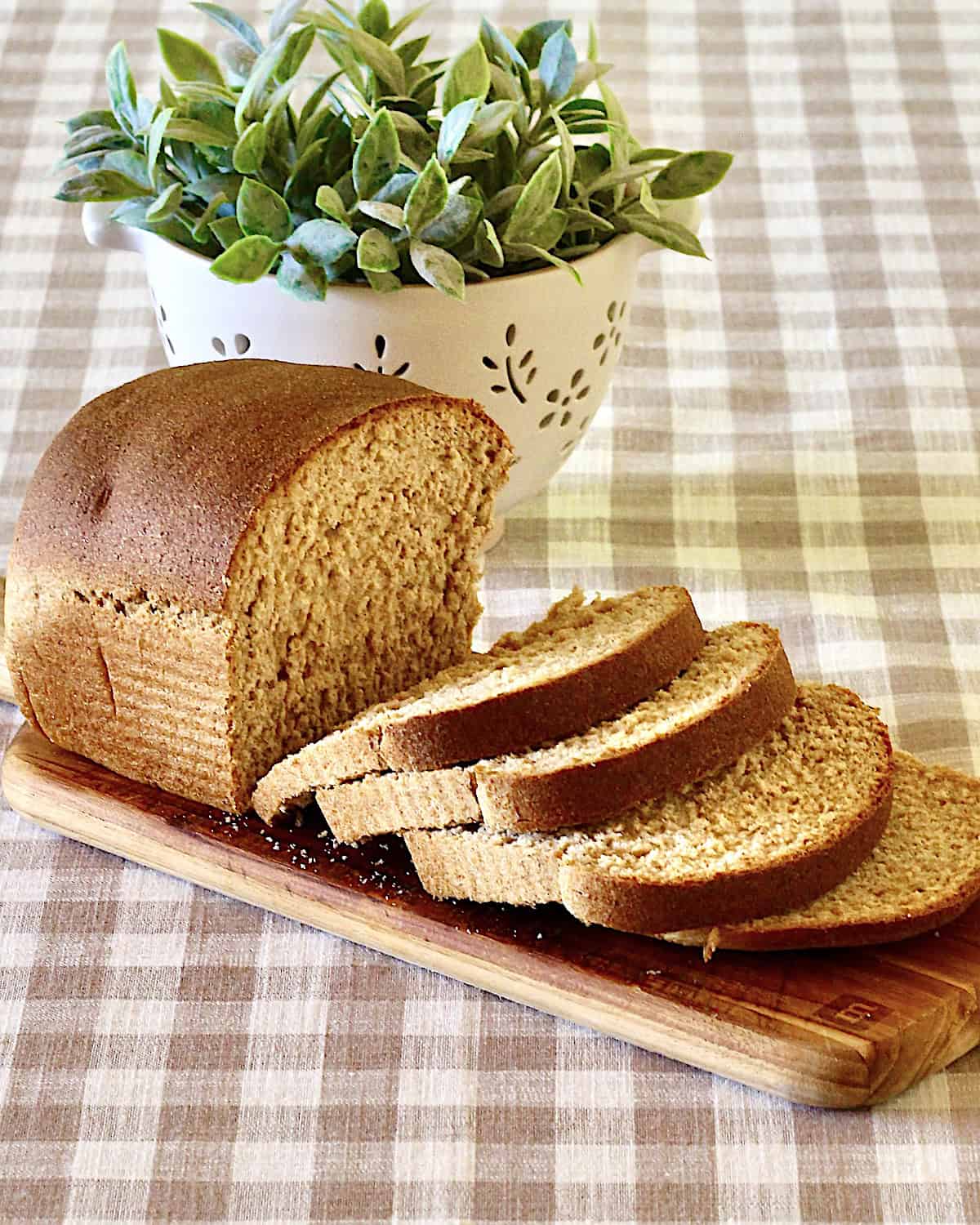 Bread loaf on checkered tablecloth in front of plant.
