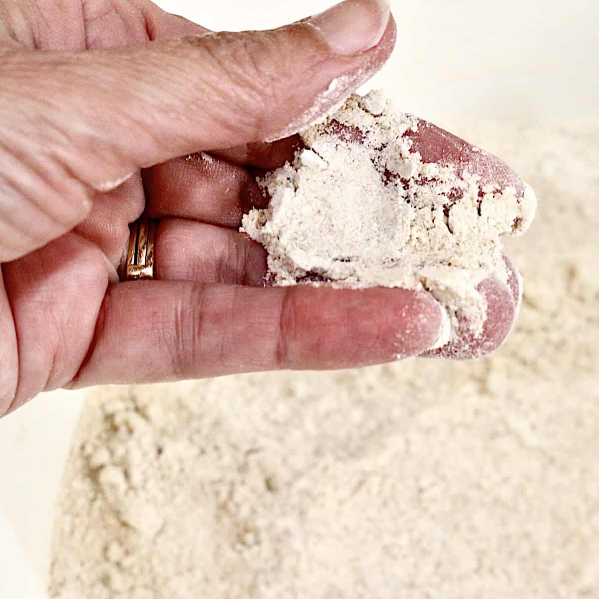 Hand holding fresh milled flour over a bowl of flour.