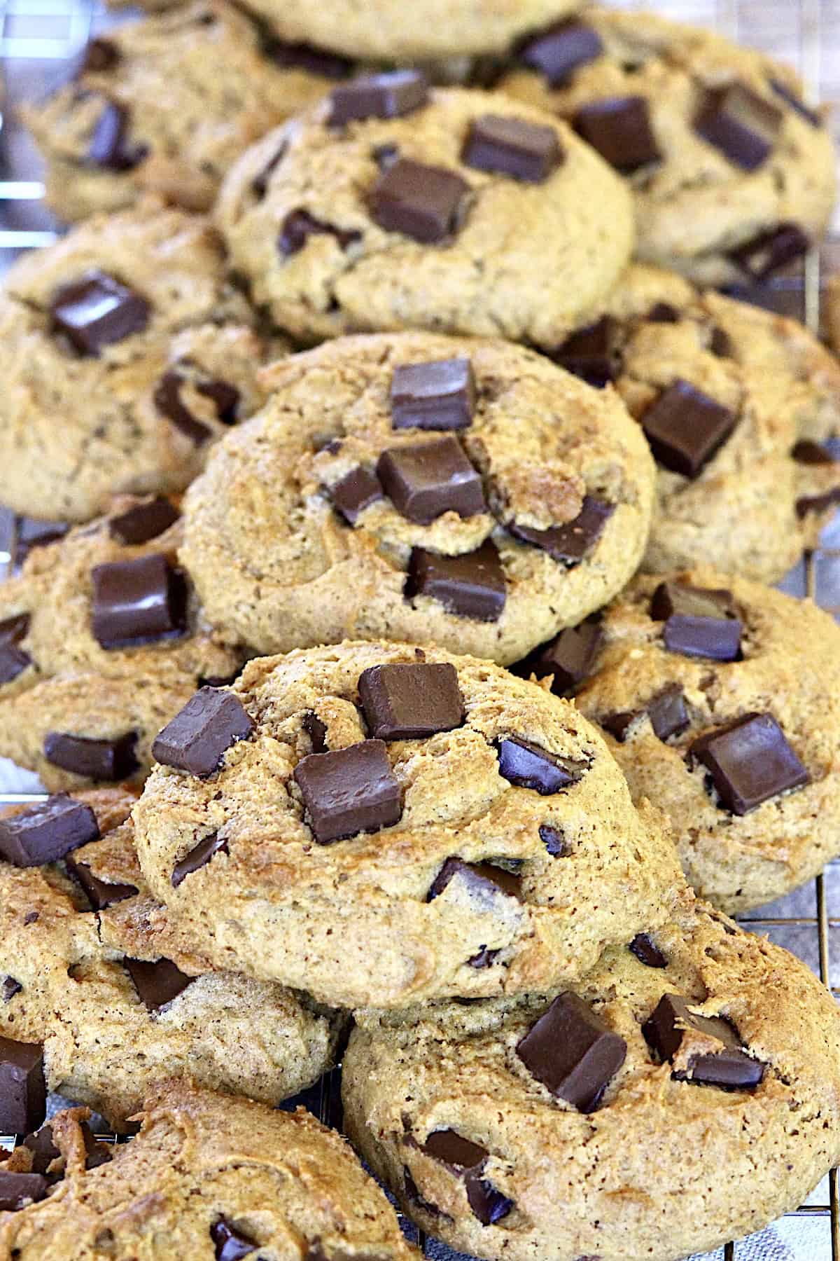 Many pumpkin chocolate chunk cookies stacked on a wire rack.